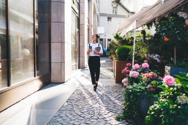 积极美丽的女人穿着休闲装在城镇的街道上散步，拿着连接4G互联网的智能手机，微笑的潮女孩拿着现代设备走在城市在夏天的晴天图片下载