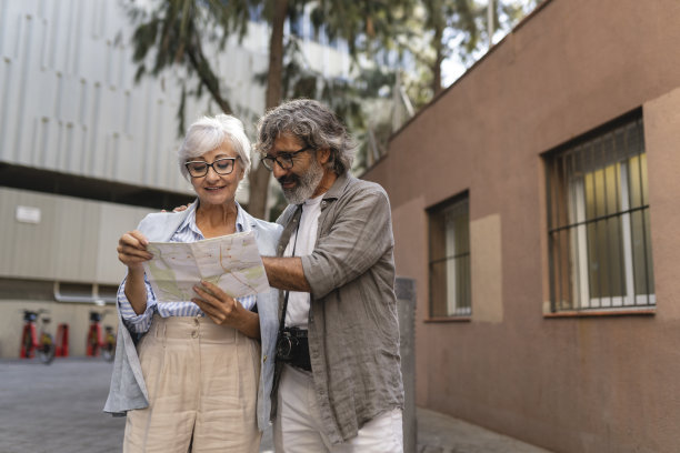 快乐的老夫妇穿着时髦的衣服一起旅行，带着城市地图寻找目的地。图片下载