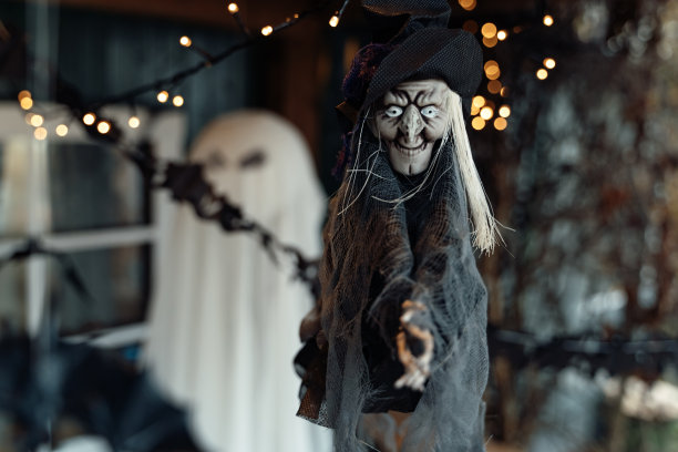 飞天扫帚上挂着可怕的玩具老女巫。闪闪发光的灯。万圣节前夕，街道上户外门廊的装饰。DIY家居、街道装饰、儿童娱乐、恐怖氛围图片下载