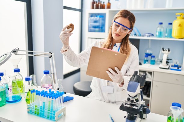 年轻的金发女人穿着科学家制服拿着猕猴桃和剪贴板在实验室图片下载