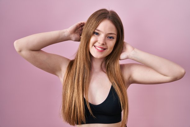 年轻的白人妇女穿着内衣在粉红色的背景下微笑与一个快乐和凉爽的微笑在脸上。显示的牙齿。图片下载