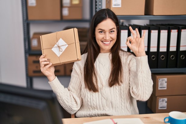 年轻的褐发女子工作在小型企业电子商务做ok的标志与手指，微笑友好的手势优秀的象征图片下载