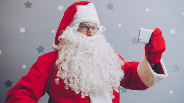 圣诞老人的肖像与智能手机相机自拍在灰色闪烁的背景图片下载