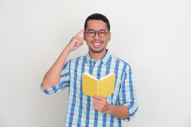 成年亚洲男子拿着一本书，用快乐的表情指着自己的大脑图片下载