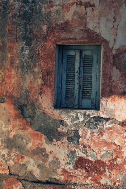 风化的粉红色石膏墙与关闭的蓝色木百叶窗小窗户。图片下载