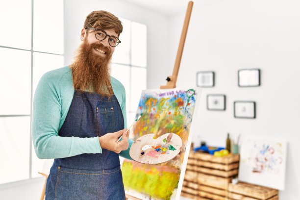年轻的红发男子微笑自信地拿着画笔和调色板在艺术工作室图片下载