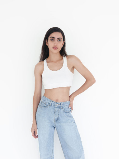 年轻美丽的女人长黑色波浪头发穿白色露脐上衣和蓝色牛仔裤苗条苗条华丽的时装模特工作室肖像图片下载