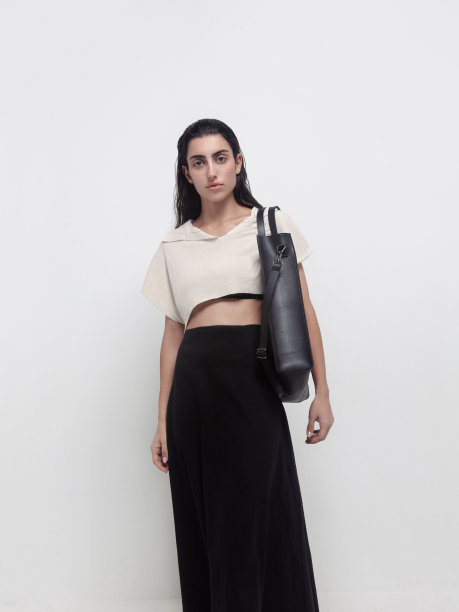 年轻美丽的黑发女人穿着优雅的衣服米色象牙色针织露脐上衣黑色及地长裙手提包在肩膀上时尚模特工作室肖像在白光背景图片下载