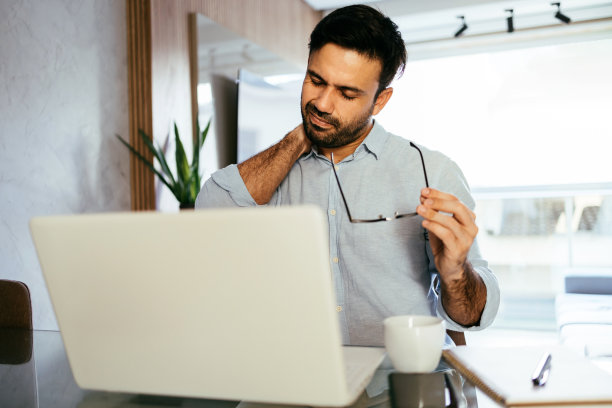 在家使用笔记本电脑工作的男子颈部疼痛图片下载