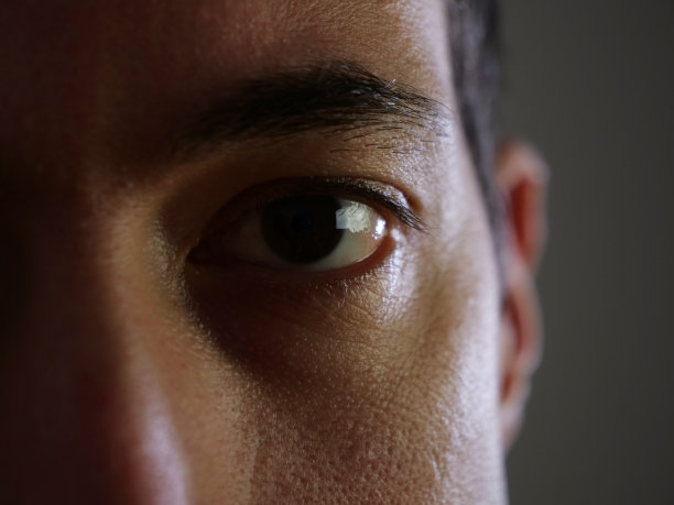 近景一个年轻人的脸在阴影中，眼睛在前景的黑色和黑暗的环境，沉思的表情在黑暗中图片下载