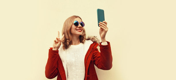 画像快乐微笑的年轻女子用智能手机自拍穿着红色夹克和皮草兜帽图片下载