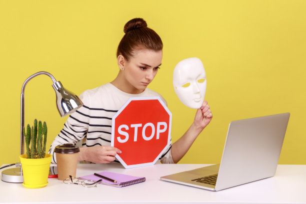 严肃的女人拿着白色面具，不知名的脸和红色交通标志，在笔记本电脑显示。图片下载