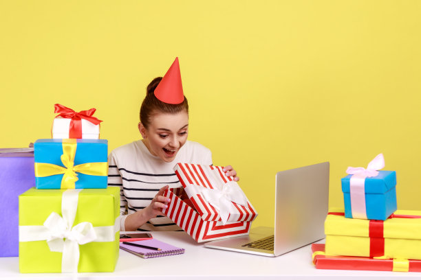 女人坐在办公室工作场所，打开礼品盒，看着里面惊喜的表情图片下载