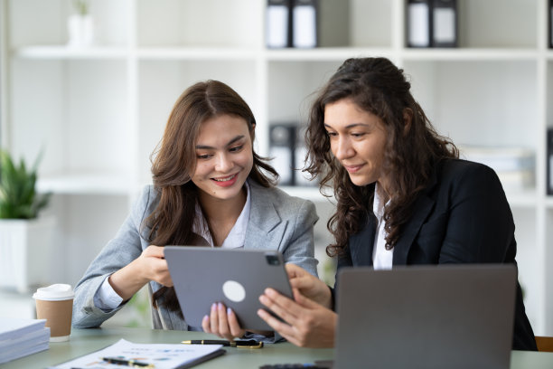 快乐的年轻女企业家在办公室的工作场所浏览平板电脑和笔记本电脑。图片下载