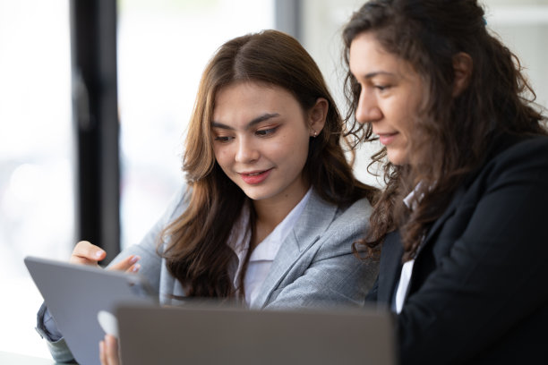 快乐的年轻女企业家在办公室的工作场所浏览平板电脑和笔记本电脑。图片下载