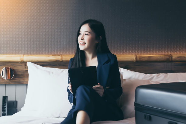 商务技术互联网酒店度假概念年轻的女商人在出差时从酒店房间工作，亚洲女性坐在床上，使用数字平板电脑预订机票快乐的女士享受生活图片下载