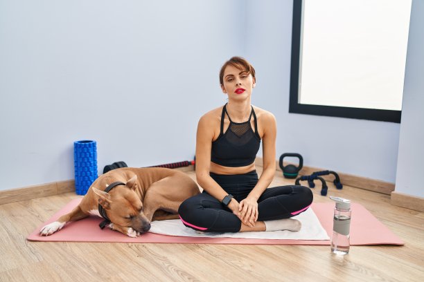 年轻美丽的女子坐在瑜伽垫上放松，严肃的表情在脸上。简单自然地看着镜头。图片下载