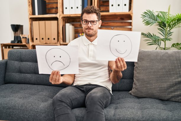 年轻的西班牙裔男子工作在抑郁症中，抱着悲伤到快乐的情绪纸怀疑和紧张，眉头紧锁，因为问题心烦意乱。消极的人。图片下载