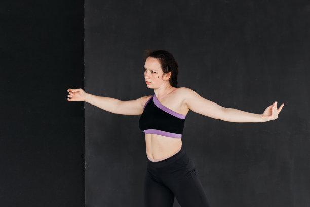 一个漂亮的棕发女孩跳现代舞。黑暗的背景。光滑的身体动作。一个年轻的运动女性的工作室肖像。女性的概念。图片下载