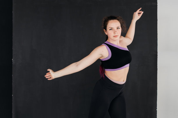 一个漂亮的棕发女孩跳现代舞。黑暗的背景。光滑的身体动作。一个年轻的运动女性的工作室肖像。女性的概念。图片下载