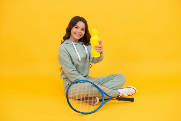 小孩拿着球拍和水瓶坐着。拿着网球拍的小孩。少女喝水图片下载