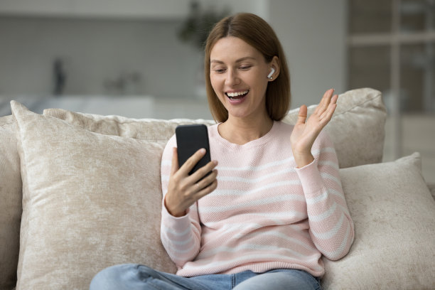 微笑的女人戴着无线耳机享受视频通话使用手机图片下载