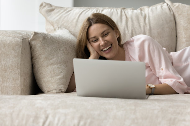 快乐的女人喜欢躺在沙发上用笔记本电脑上网图片下载
