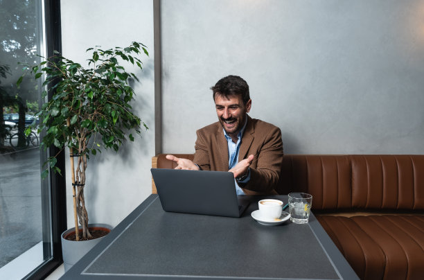 年轻的商人，自由职业者，金融专家利用他的午餐和咖啡休息时间与他满意的客户在笔记本电脑上视频通话谈论工作。商务人员与办公室团队的对话图片下载