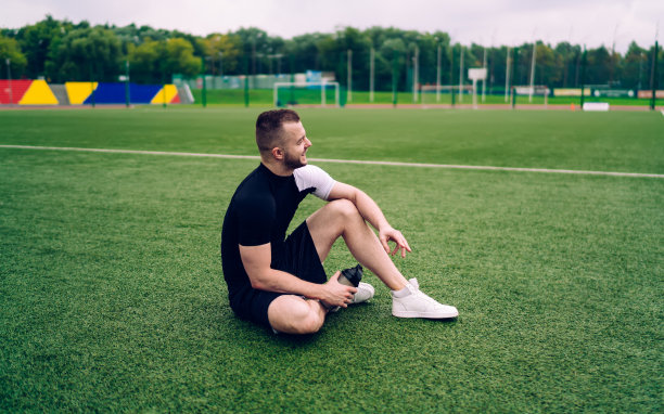 年轻肌肉发达的运动员坐在绿色的体育场草坪上笑图片下载
