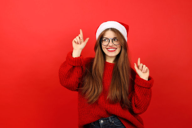 在庆祝新年的时候，一个红色背景的穿着新年毛衣的快乐的女人指着上面。图片下载