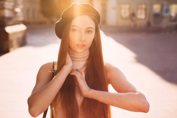性感的照片，一个女孩在黑色贝雷帽看着相机镜头对建筑和阳光的背景图片下载