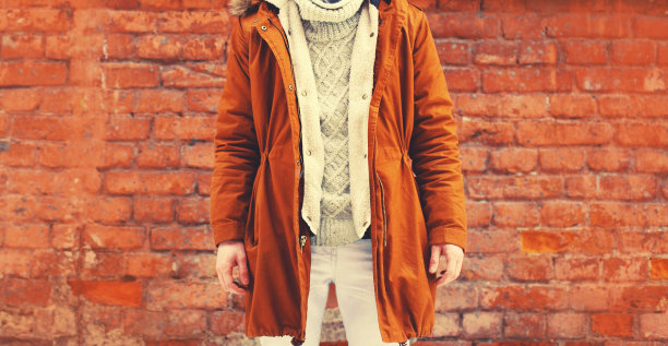 特写时尚的年轻人穿着棕色夹克，针织毛衣在城市的纹理砖墙背景图片下载