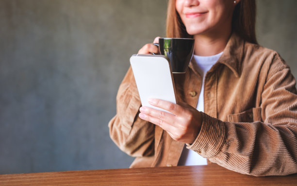 一个年轻女子在喝咖啡时手持并使用手机的特写图片图片下载