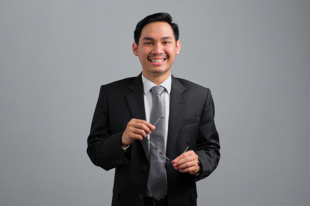 画像微笑英俊的年轻商人在正式的西装感觉轻松和自信，看着相机孤立的灰色背景图片下载