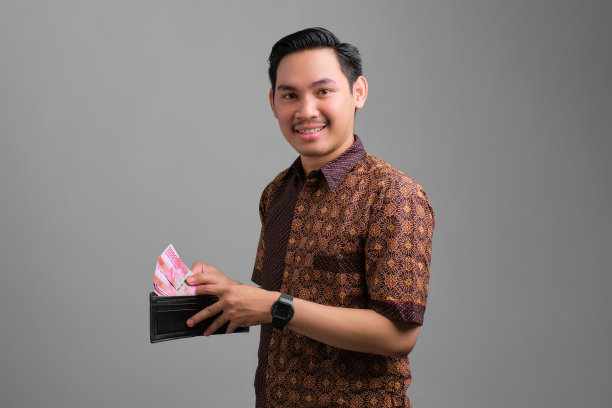肖像微笑年轻的亚洲人穿着蜡染衬衫从他的钱包纸钱孤立在灰色背景图片下载