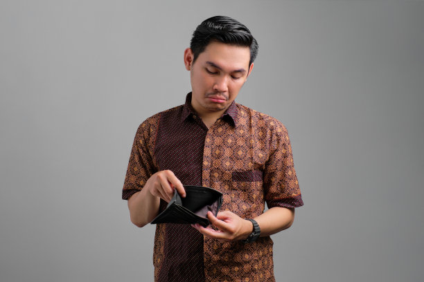 肖像不快乐的年轻亚洲人穿着蜡染衬衫看空钱包孤立在灰色背景图片下载