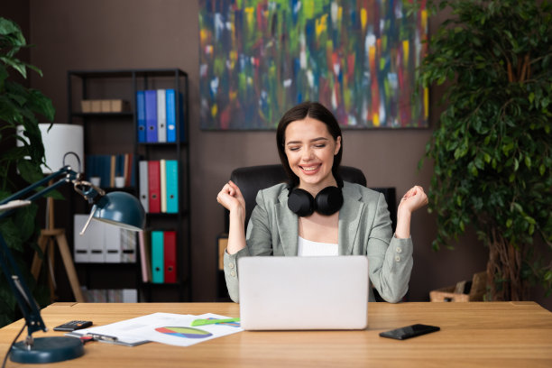 兴奋愉快的微笑着的女人，穿着时髦的西装，戴着耳机坐在家里的办公桌前，在家在线工作，庆祝面试后的成功图片下载