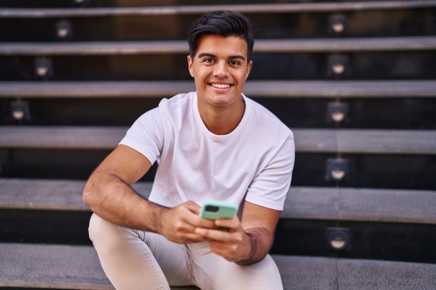 年轻的西班牙男子坐在街道的楼梯上使用智能手机图片下载