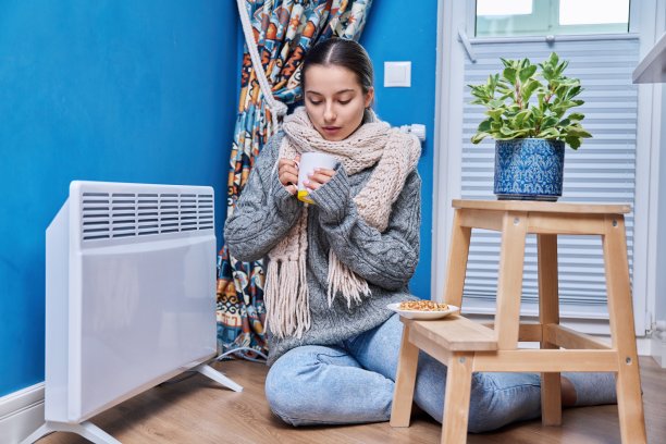 十几岁的女性围着毛衣围巾取暖，旁边是电热暖气片，喝着热饮图片下载