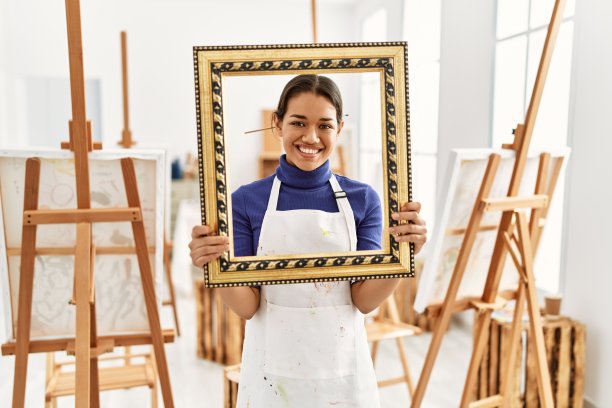 年轻的拉丁妇女微笑自信地拿着空框架在艺术工作室图片下载