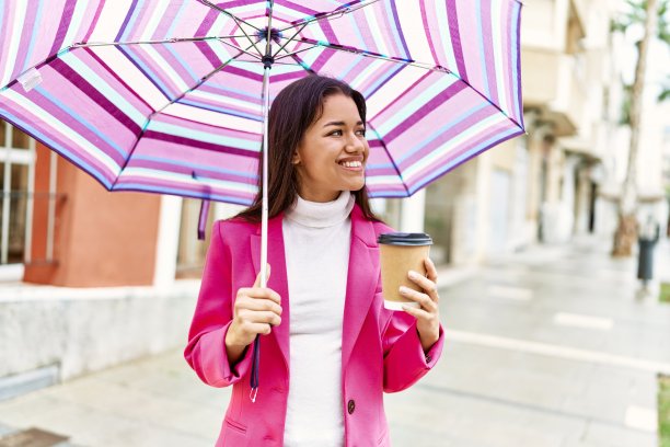 年轻的拉丁女子在街上打着伞喝咖啡图片下载