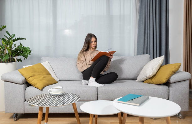 人们和休闲观念——年轻女子在家里的沙发上看书，享受她在家里学习和工作的空闲时间。图片下载