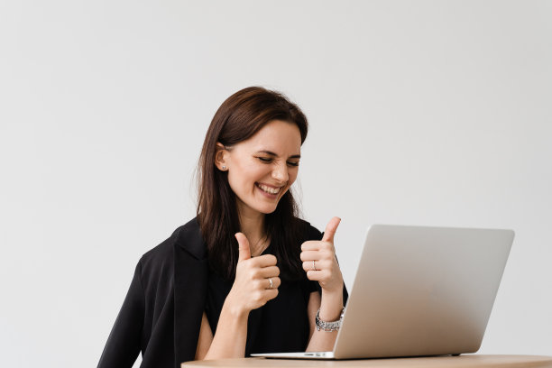 快乐的女孩用笔记本电脑和朋友视频交流时竖起大拇指。成功的商业女性远程工作，在在线视频会议中与同事一起大笑。图片下载