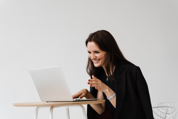 视频会议与朋友和同事和乐趣远程在线后成功的项目。带着笔记本电脑微笑的女孩，笑着和同事讨论工作中有趣的情况。图片下载