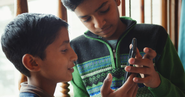 浅聚焦两个印度兄弟在手机上浏览他们的自拍照片图片下载