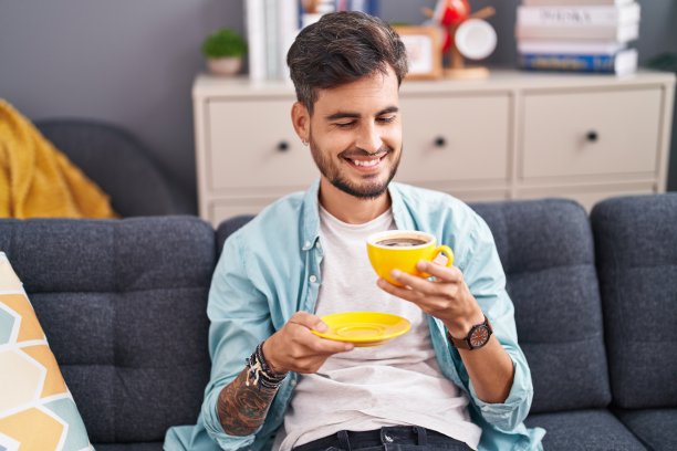 年轻的西班牙人坐在家里的沙发上喝咖啡图片下载