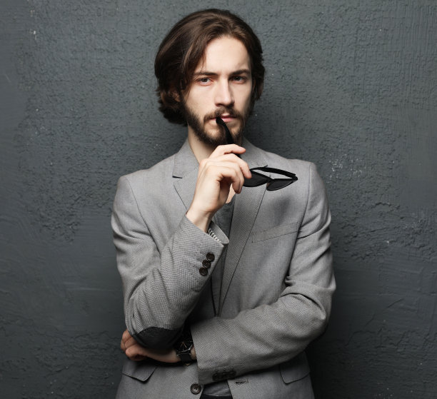 年轻的胡子男，时尚的发型和胡子看着相机在灰色的背景图片下载