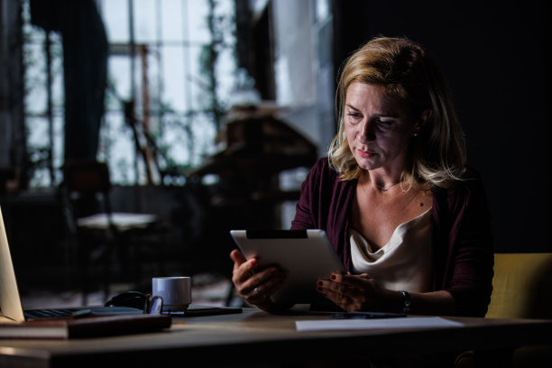 一位女士坐在家里的办公桌前，使用着一个数字平板电脑图片下载