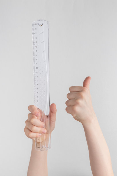 儿童手握透明玻璃或塑料尺子，竖起大拇指。白色和灰色背景与复制空间图片下载