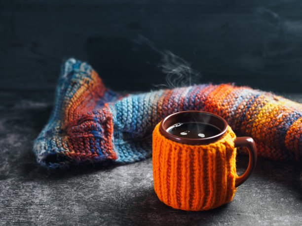 一杯穿着橙色针织夹克的热咖啡。暖暖的五彩秋色围巾。图片下载